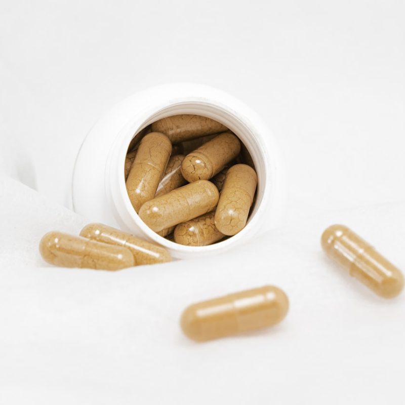 Natural supplement capsules spilling from a white bottle with green herbs — clean label lubricant